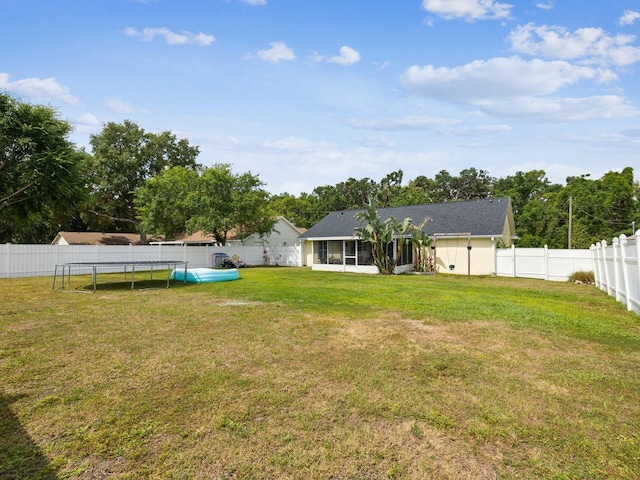 view of yard with a fenced backyard, a sunroom, and a trampoline