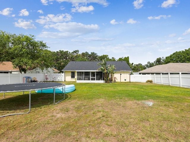 view of yard with a fenced backyard, a sunroom, and a trampoline