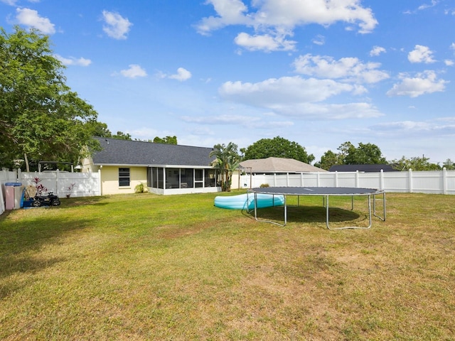 view of yard featuring a trampoline, a sunroom, and a fenced backyard