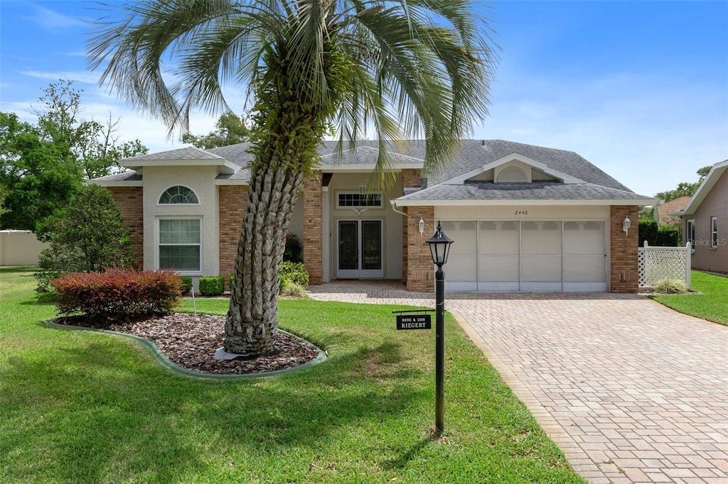 view of front of home featuring roof with shingles, decorative driveway, a front lawn, brick siding, and a garage