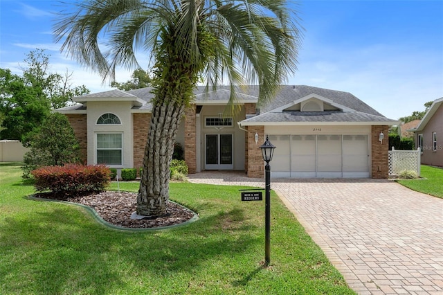 view of front of home featuring roof with shingles, decorative driveway, a front lawn, brick siding, and a garage
