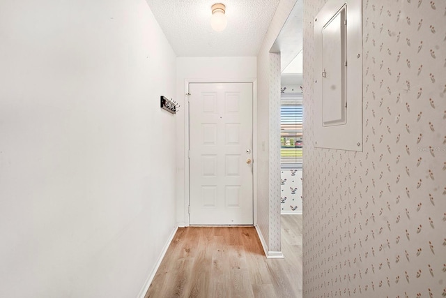 doorway with light wood-type flooring, electric panel, baseboards, and a textured ceiling