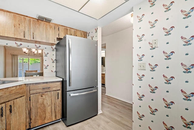 kitchen with light wood finished floors, visible vents, freestanding refrigerator, a chandelier, and light countertops