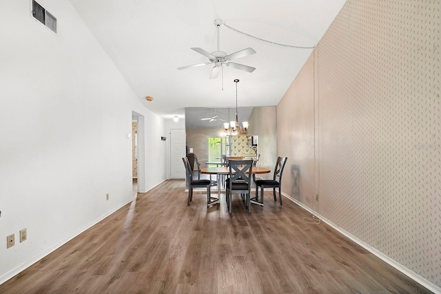 dining space featuring wallpapered walls, wood finished floors, visible vents, and ceiling fan with notable chandelier