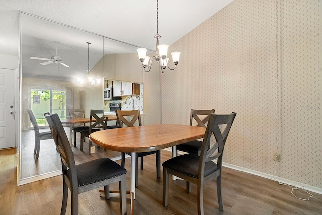 dining area with ceiling fan with notable chandelier, wallpapered walls, vaulted ceiling, and wood finished floors