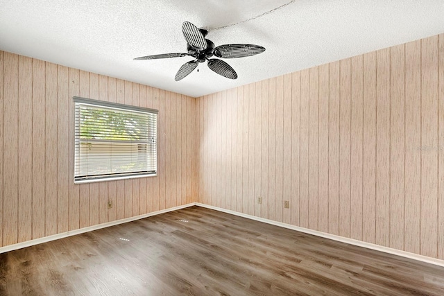 spare room featuring a ceiling fan, wood finished floors, a textured ceiling, wooden walls, and baseboards