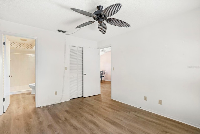 unfurnished bedroom with wood finished floors, a closet, ensuite bath, baseboards, and visible vents