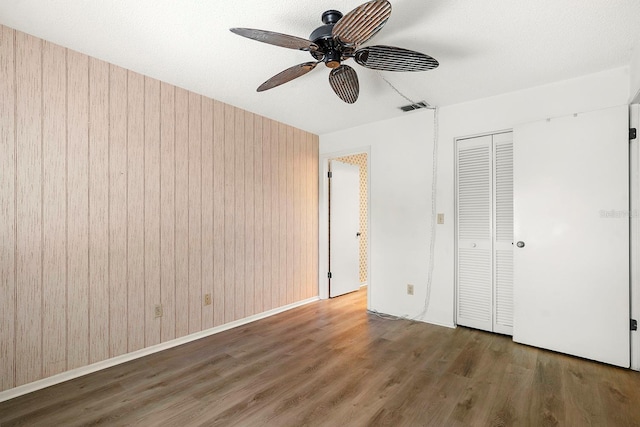 unfurnished bedroom featuring a ceiling fan, wood finished floors, a closet, wooden walls, and visible vents