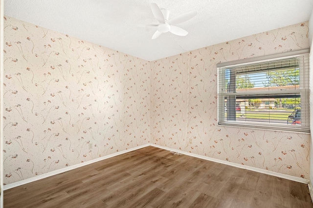 unfurnished room with a textured ceiling, baseboards, wallpapered walls, wood finished floors, and ceiling fan