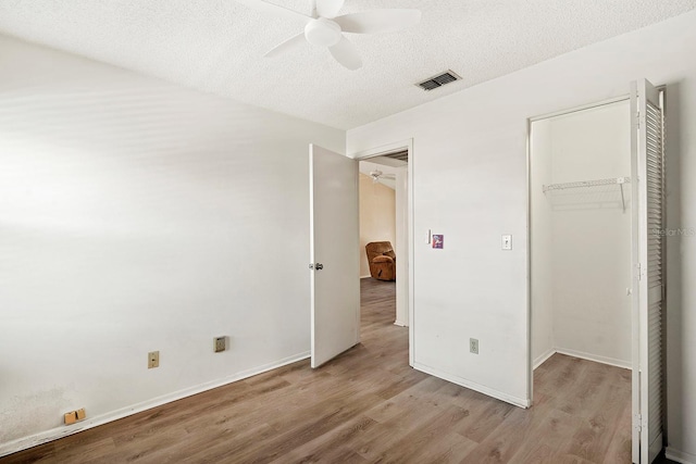 unfurnished bedroom featuring a textured ceiling, visible vents, a ceiling fan, wood finished floors, and a closet