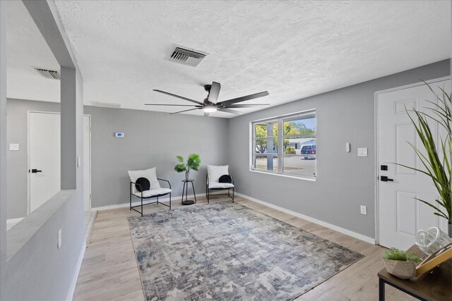 4607 Kennedy Dr, New Port Richey, FL 34652 - living area featuring a ceiling fan, a textured ceiling, light wood-style flooring, baseboards, and visible vents
