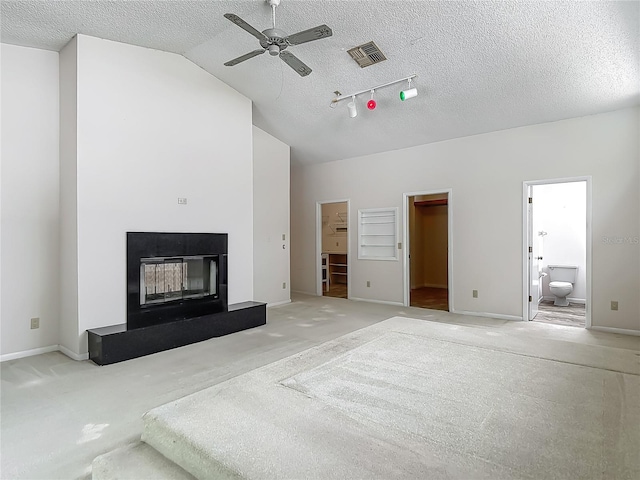 unfurnished living room with visible vents, a glass covered fireplace, a textured ceiling, carpet flooring, and ceiling fan
