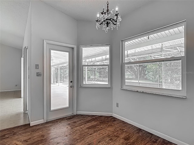 unfurnished dining area with wood finished floors, baseboards, an inviting chandelier, and a textured ceiling