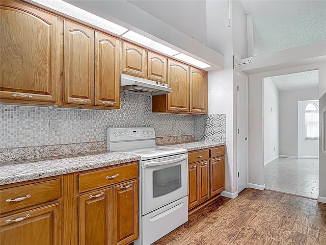 kitchen with dark wood-style floors, backsplash, brown cabinets, under cabinet range hood, and electric stove