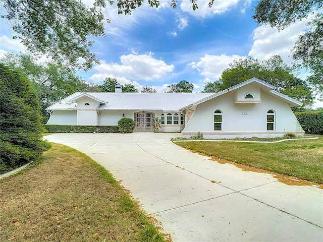 single story home featuring a chimney, driveway, a front yard, metal roof, and stucco siding