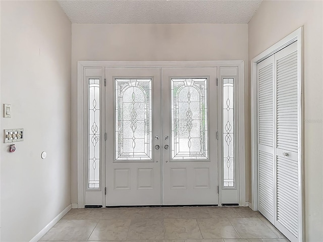 entryway featuring baseboards, french doors, a textured ceiling, and light tile patterned floors