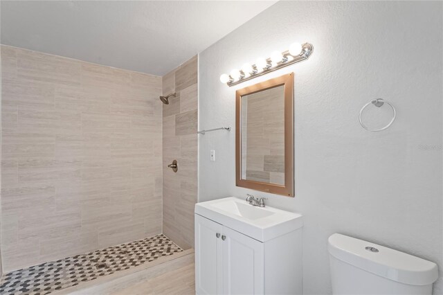full bath featuring a tile shower, toilet, and vanity