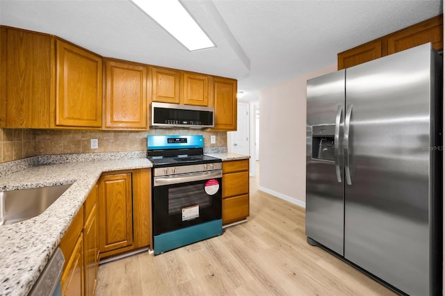 7321 Parrot Dr, Port Richey, FL 34668 - kitchen featuring light stone counters, tasteful backsplash, brown cabinetry, stainless steel appliances, and light wood finished floors