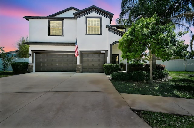 view of front of property featuring driveway, stone siding, fence, a garage, and stucco siding