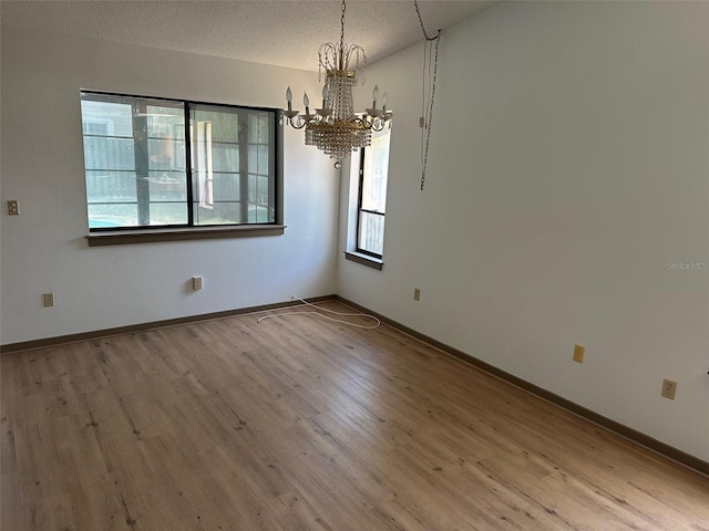 1412 Wexford Dr N, Palm Harbor, FL 34683 - empty room featuring baseboards, a textured ceiling, a notable chandelier, and wood finished floors