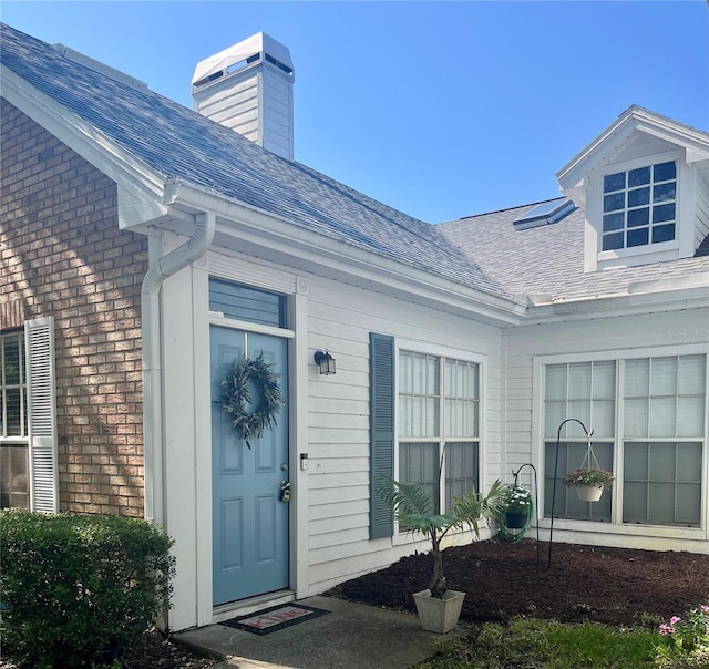 2729 Penzance St, Palm Harbor, FL 34684 - entrance to property featuring a shingled roof, a chimney, and brick siding