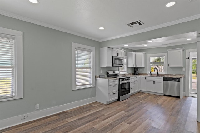 kitchen featuring wood finished floors, a sink, stainless steel appliances, white cabinets, and visible vents