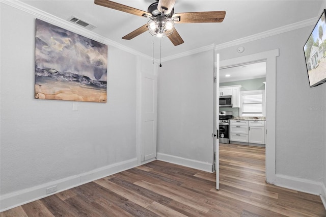 empty room with baseboards, visible vents, wood finished floors, ceiling fan, and ornamental molding