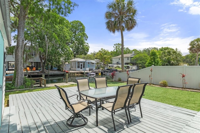 wooden deck with a fenced backyard, a water view, outdoor dining space, and a lawn