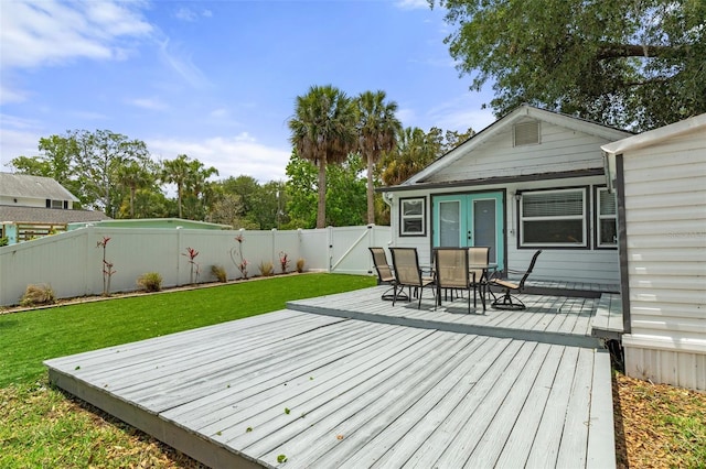 deck with a fenced backyard, a gate, outdoor dining space, and a lawn