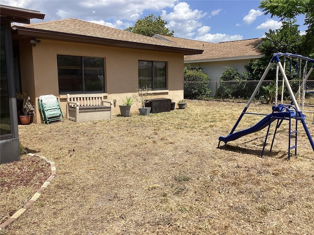 13111 Sheridan Dr, Hudson, FL 34667 - rear view of house featuring a playground, stucco siding, and a shingled roof