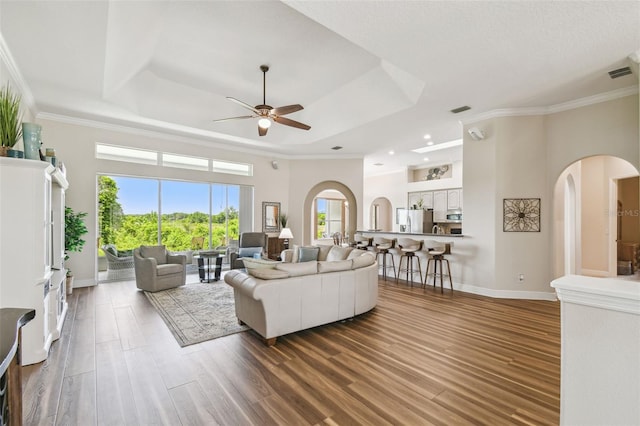 living area featuring arched walkways, a ceiling fan, visible vents, and a tray ceiling