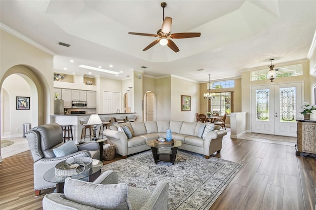 living room with arched walkways, wood finished floors, baseboards, ceiling fan with notable chandelier, and a tray ceiling