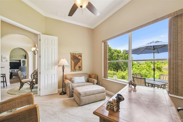 living area featuring arched walkways, ceiling fan, ornamental molding, and light carpet