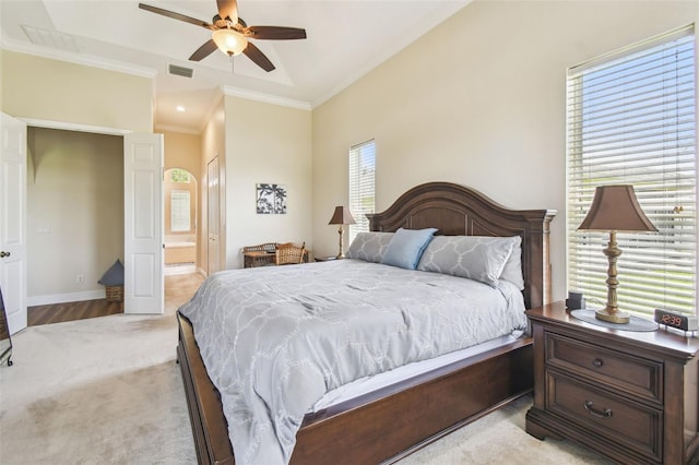 bedroom featuring ceiling fan, light colored carpet, ensuite bath, visible vents, and ornamental molding