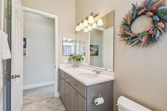 bathroom featuring double vanity, toilet, baseboards, and a sink