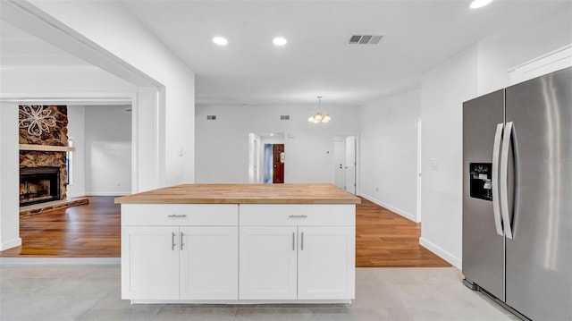 kitchen with white cabinets, light wood finished floors, stainless steel fridge with ice dispenser, wood counters, and visible vents