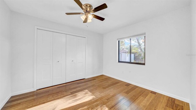 unfurnished bedroom featuring baseboards, a ceiling fan, wood finished floors, and a closet