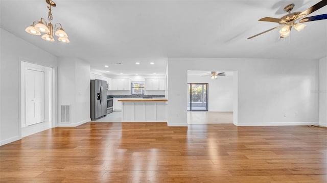 unfurnished living room featuring baseboards, ceiling fan with notable chandelier, light wood-style flooring, and visible vents