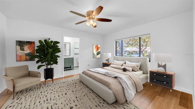 bedroom featuring a ceiling fan, baseboards, ensuite bathroom, and light wood-type flooring