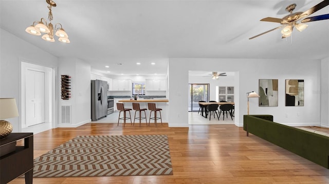 living room with baseboards, visible vents, ceiling fan with notable chandelier, and light wood-type flooring
