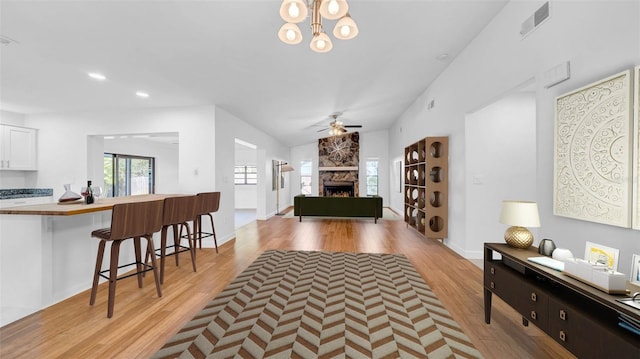living area featuring visible vents, light wood-style floors, a stone fireplace, recessed lighting, and ceiling fan with notable chandelier