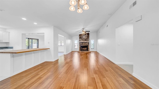 unfurnished living room with a fireplace, ceiling fan with notable chandelier, light wood-style flooring, and visible vents