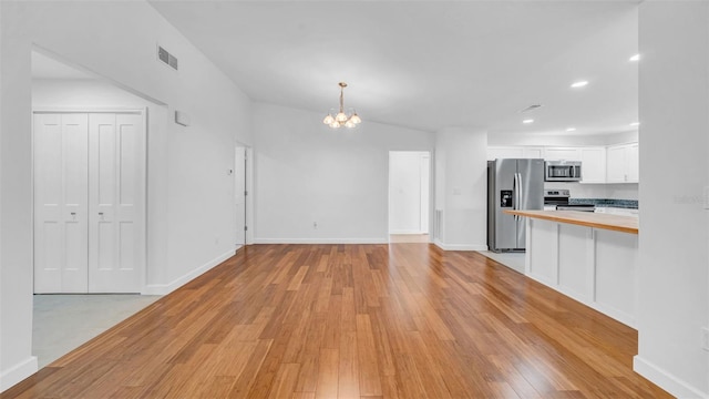 unfurnished living room with visible vents, light wood finished floors, and a notable chandelier