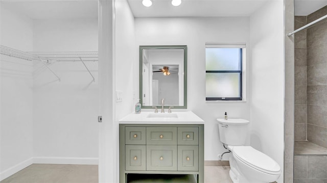 bathroom with toilet, baseboards, a tile shower, and vanity