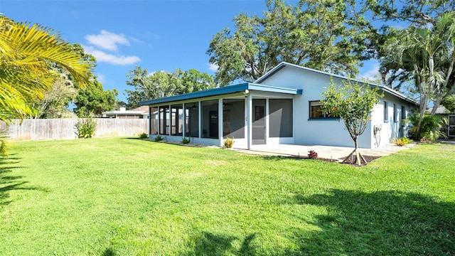 back of property with a sunroom, stucco siding, fence, and a yard