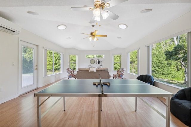 game room featuring a wall mounted air conditioner, wood finished floors, vaulted ceiling, and plenty of natural light