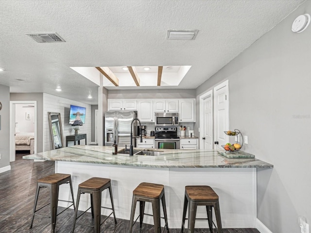 kitchen with appliances with stainless steel finishes, visible vents, a kitchen breakfast bar, and a sink