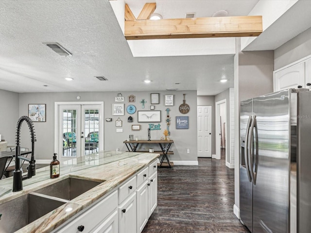 kitchen with a sink, baseboards, dark wood-style flooring, light stone countertops, and stainless steel fridge