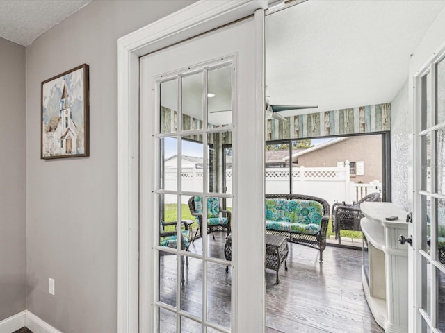 doorway with a textured ceiling, ceiling fan, wood finished floors, and baseboards