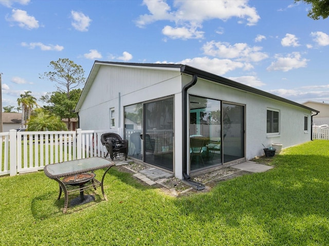 rear view of house with stucco siding, a sunroom, and a lawn